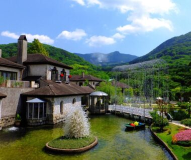 Pond with central fountain, riverside ryokan buildings, small bridge and mountain backdrop at Fukushimakan in Kanagawa