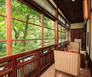 Wooden lounge with chairs facing verdant garden through large wooden-framed windows at Fukuzumiro, Kanagawa