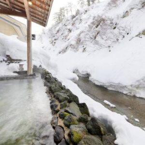 Outdoor stone onsen bath with steam and snow banks at Fulsato ryokan, Iwate Tōhoku