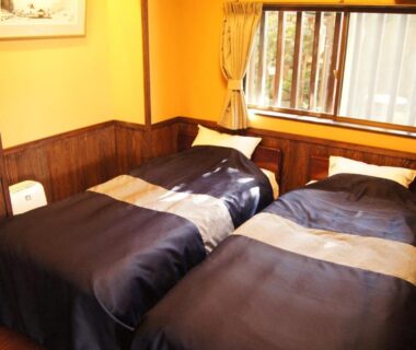 Twin beds with dark linens, wooden paneling and curtained window in Fumoto Ryokan room, Kumamoto, Kyūshū