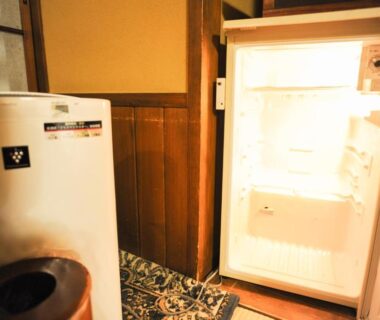 Open mini refrigerator in traditional wooden ryokan hallway with patterned mat and small waste bin