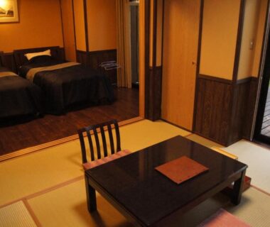 Tatami room with low table, twin beds and sliding doors to a small garden at Fumoto Ryokan, Kumamoto
