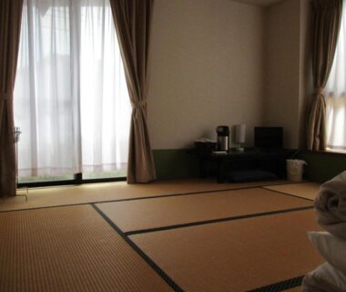 Traditional tatami room with folded futon, low table, small kettle and sheer curtains at Funayado Akitaya, Kanagawa