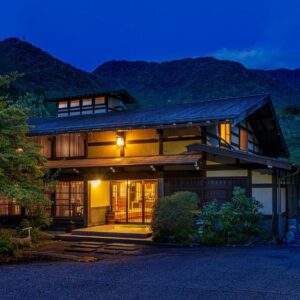 Traditional illuminated ryokan entrance with mountain backdrop in Gifu Chūbu, Japan
