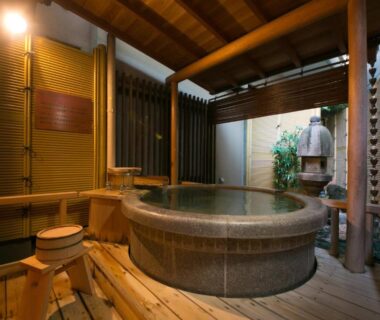 Round stone onsen bath on wooden deck with stools and bamboo screens at Furuya Ryokan, Shizuoka