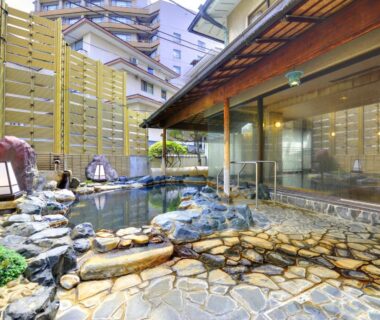 Stone outdoor onsen with rock-lined pool beside wooden ryokan building in Shizuoka