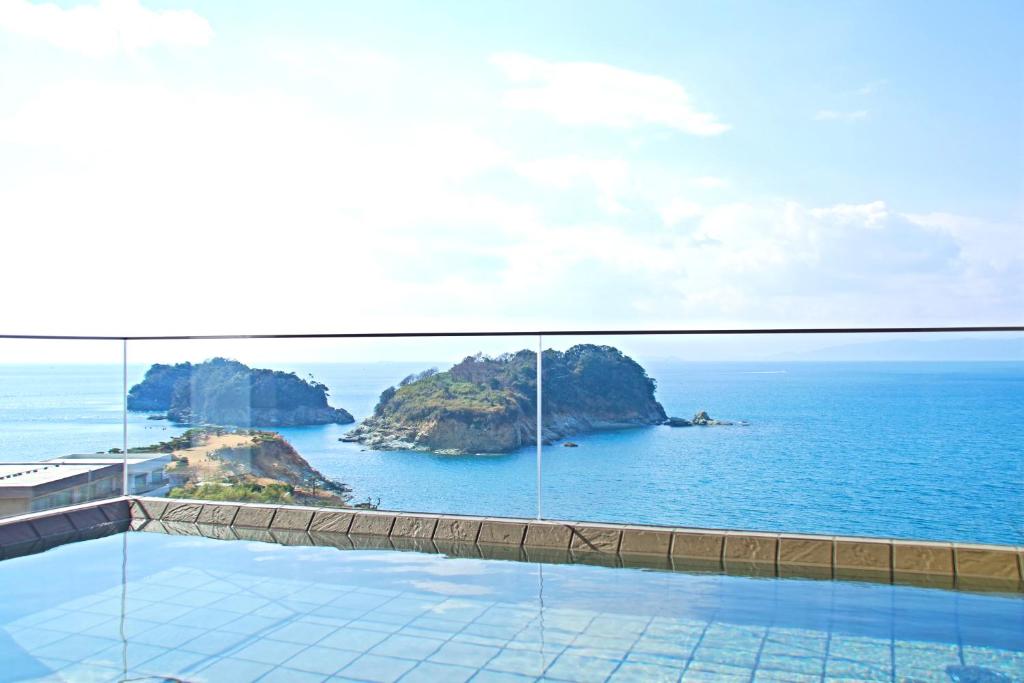 Seaside onsen at Futagojimasou Wakayama Outdoor onsen bath with tiled edge and glass railing overlooking islands and blue sea at Futagojimasou, Wakayama