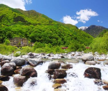 Rocky mountain river foreground with Futari Shizuka building and green hills in Nagano Chūbu