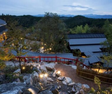 Evening view of stone steps, wooden bridge and lit guesthouses at Gekkoju Kurokawa in Kumamoto, Kyushu