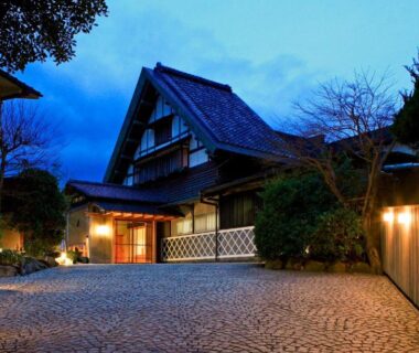 Cobblestone approach and lit wooden entrance of Genmyoan ryokan in Kyoto with traditional gabled roof