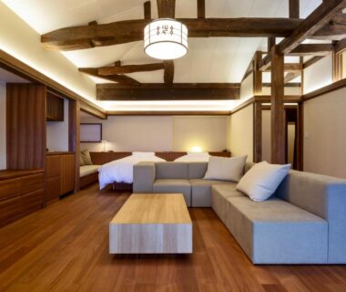Calm ryokan interior with exposed wooden beams, sofa, low table, hardwood floor and twin beds in Kyoto