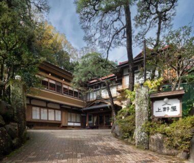Traditional wooden ryokan entrance with stone sign and surrounding trees at Gensen Uenoya in Kanagawa