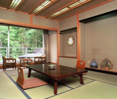 Traditional tatami room with low table, floor cushions, tokonoma alcove and balcony overlooking greenery