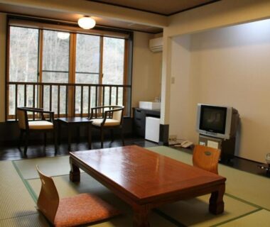Traditional tatami room with low wooden table, floor cushions and window seating overlooking trees