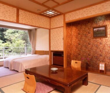 Tatami room with low wooden table, zaisu chairs, twin beds and balcony overlooking greenery at Gensenkan Tochigi