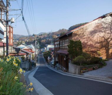 Narrow paved street lined with traditional wooden ryokan buildings, planters and hillside backdrop in Nagano, Chūbu