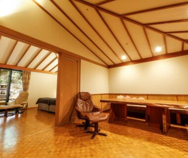 Spacious wooden interior with low table, reclining chair and sliding doors to garden at Ginsuisou Choraku Hyōgo