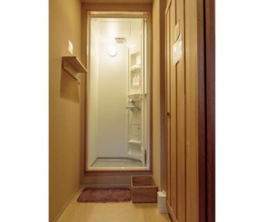 Narrow wooden corridor leading to compact shower stall with mats at Gion Ryokan Q-beh in Kyoto