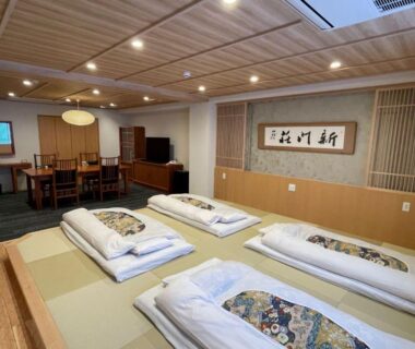 Traditional tatami room with futons, low wooden ceiling, calligraphy and small dining area at Gion Shinmonso Kyoto