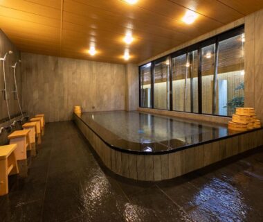 Indoor communal bathing area with rectangular soaking tub, shower stations, wooden stools and buckets at Gion Shinmonso Kyoto