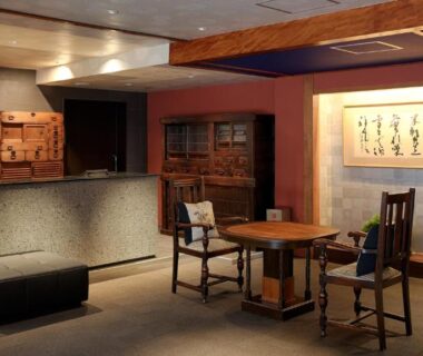 Calm ryokan reception lounge with wooden beams, low table and framed calligraphy at Gion Shinmonso Kyoto