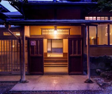 Warmly lit wooden entrance with sliding doors and stone path at Gora Kansuiro, Kanagawa