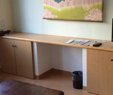 Low wooden desk and cabinets in a tatami room with wall art and small TV at Goroji Bekkan, Gunma