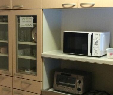 Compact kitchenette with microwave, toaster oven and glass-front cabinets at Goroji Bekkan in Gunma