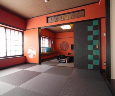 Traditional tatami room with shoji windows, low seating alcove, geometric sliding panel and warm red walls at Goyokan, Shizuoka