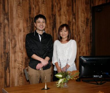 Two reception staff behind wooden desk at Granvillage Toya Daiwa Ryokan Annex in Hokkaidō, warm wood interior