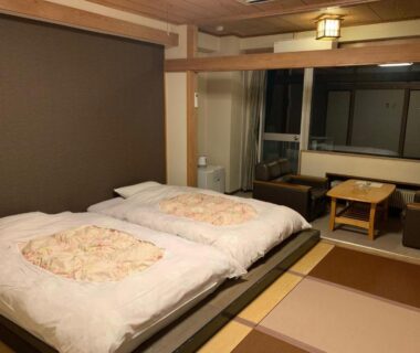 Tatami room with two futon beds, low table seating and large window at Granvillage Toya Daiwa Ryokan Annex