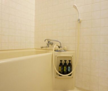 Tiled bathroom with beige bathtub, handheld shower and mounted toiletries at Green Spa Tsutsuga in Hiroshima