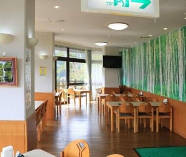 Bright dining area with wooden tables, chairs and green bamboo mural at Green Spa Tsutsuga in Hiroshima