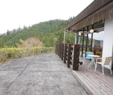 Outdoor wooden terrace with chairs and tables beside sliding doors overlooking forested hills at Green Spa Tsutsuga in Hiroshima