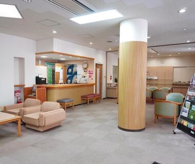 Spacious ryokan reception and seating area with wooden column, brochure stand, and check-in desk at Green Spa Tsutsuga Hiroshima