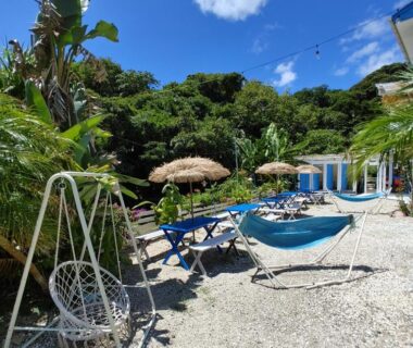 Gravel courtyard with hammocks, parasols and lounge chairs surrounded by lush trees at Guest House Churaumi Shizuoka
