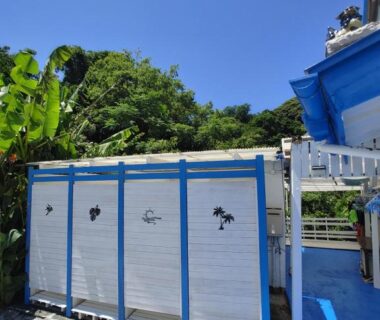 Blue-trimmed outdoor cubicles beside tropical foliage at Guest House Churaumi, Chūbu Shizuoka