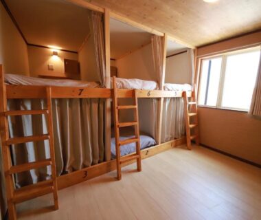 Bunk beds with wooden frames, curtains and ladder in Guest House Nemuroman room, light from window