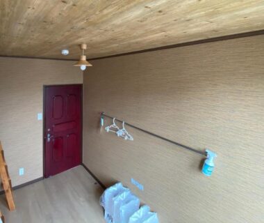 Compact room with wooden ceiling, red door and stacked bedding at Guest House Nemuroman, Hokkaidō