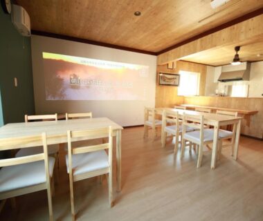 Communal wooden dining space with projection screen and kitchenette at Guest House Nemuroman Hokkaidō Japan