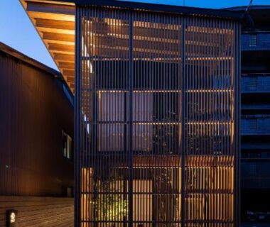 Narrow multi-story wooden frontage with vertical slats illuminated at dusk, entrance of Gunjo no Tsuki in Ishikawa, Chūbu