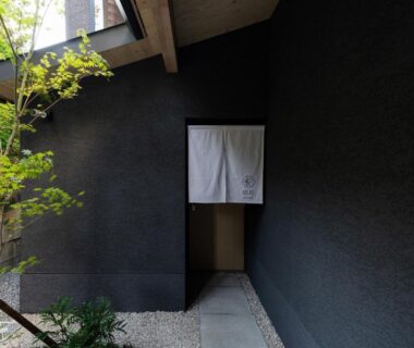 Noren entrance with stone path and textured dark wall at Gunjo no Tsuki in Ishikawa