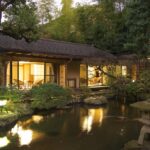 Traditional ryokan beside reflective garden pond with stone lantern and lit shoji rooms in Kanagawa