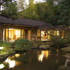 Traditional ryokan beside reflective garden pond with stone lantern and lit shoji rooms in Kanagawa
