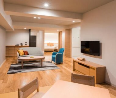 Open-plan guest room with wooden flooring, sofa seating, dining table and TV at HAKODATE Uminokaze Hokkaidō