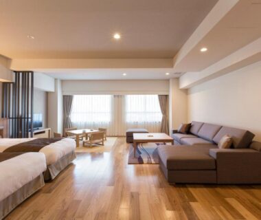 Large wood-floored twin room with sofa, table and wide windows at HAKODATE Uminokaze Hokkaidō