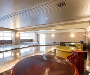 Large tiled indoor bathing area with wooden tubs at HAKODATE Uminokaze Hokkaidō Japan