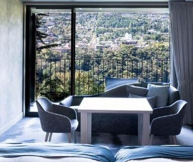 Modern guest room with low beds, seating area and large window overlooking Kanagawa city