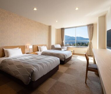Modern twin bedroom with two single beds, desk and large window overlooking distant mountains in Kanagawa