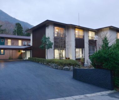 Two-story guest house with lit windows, paved driveway and mountain backdrop in Hakone, Kanagawa